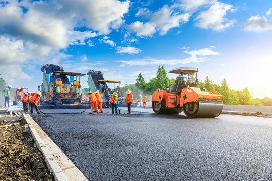 Asphalt paver laying fresh asphalt at sunset